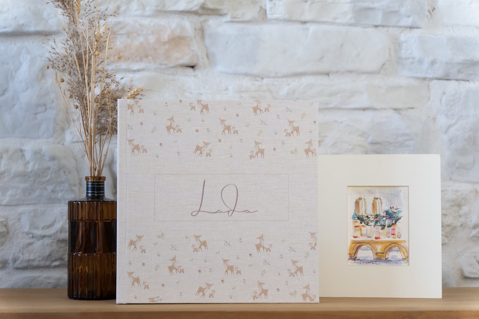 An ivory linen book with small illustrated fawns and a name written on the cover.