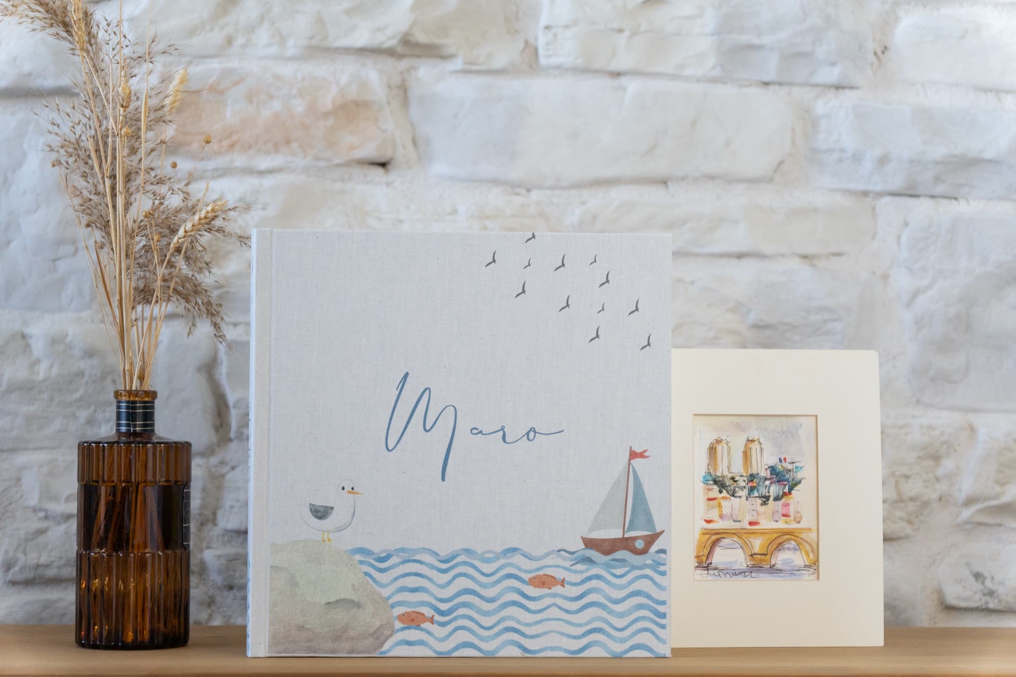 A cream book with an illustrated sailboat on the cover and a name written beneath it.